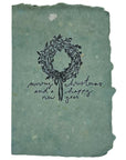 Christmas card with dark tree wreath and “Merry Christmas” lettering on teal paper