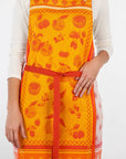 Orange fruit jacquard apron with front pocket panel and vertical red tie at waist.