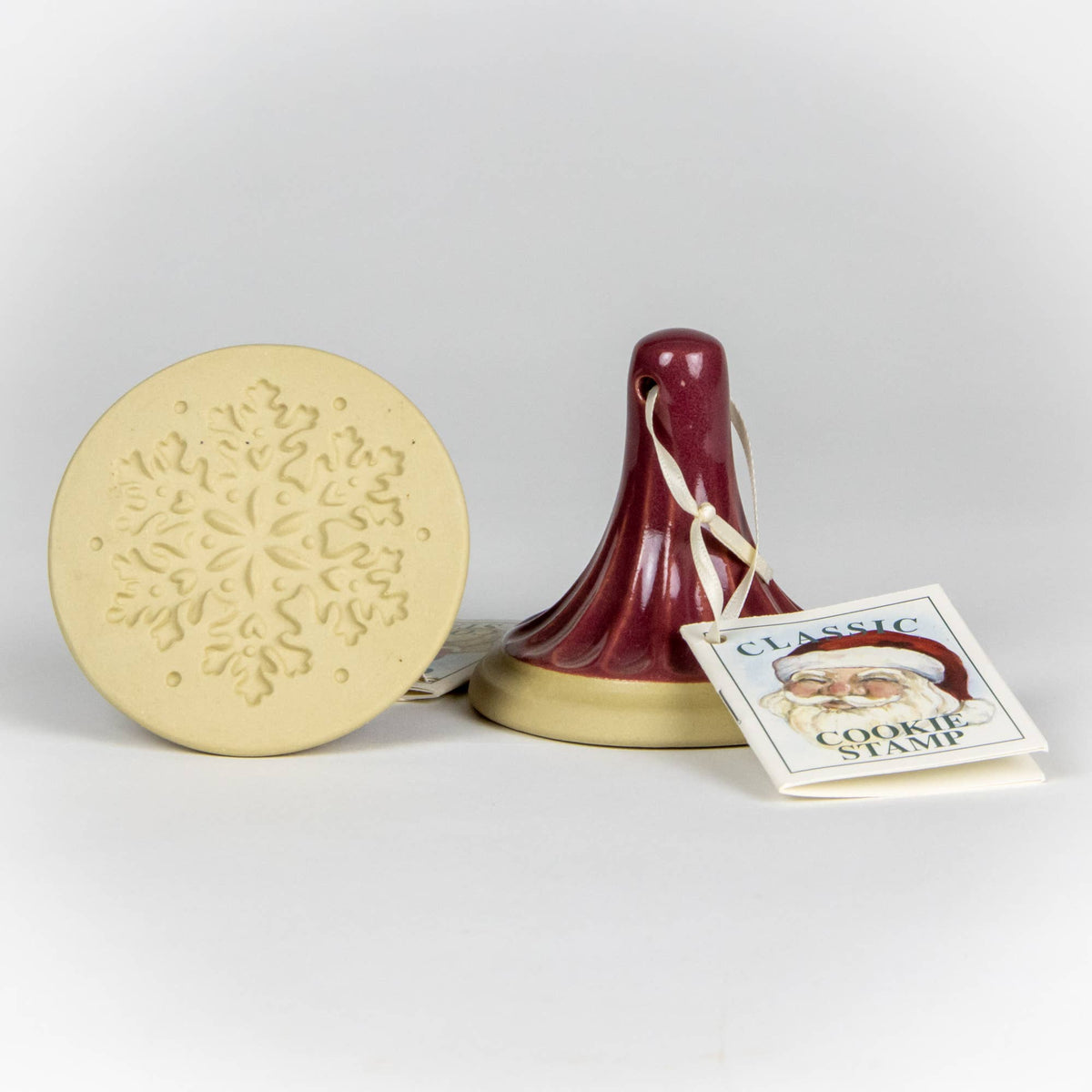 Snowflake cookie stamp: beige disc with embossed snowflake pattern and burgundy handle