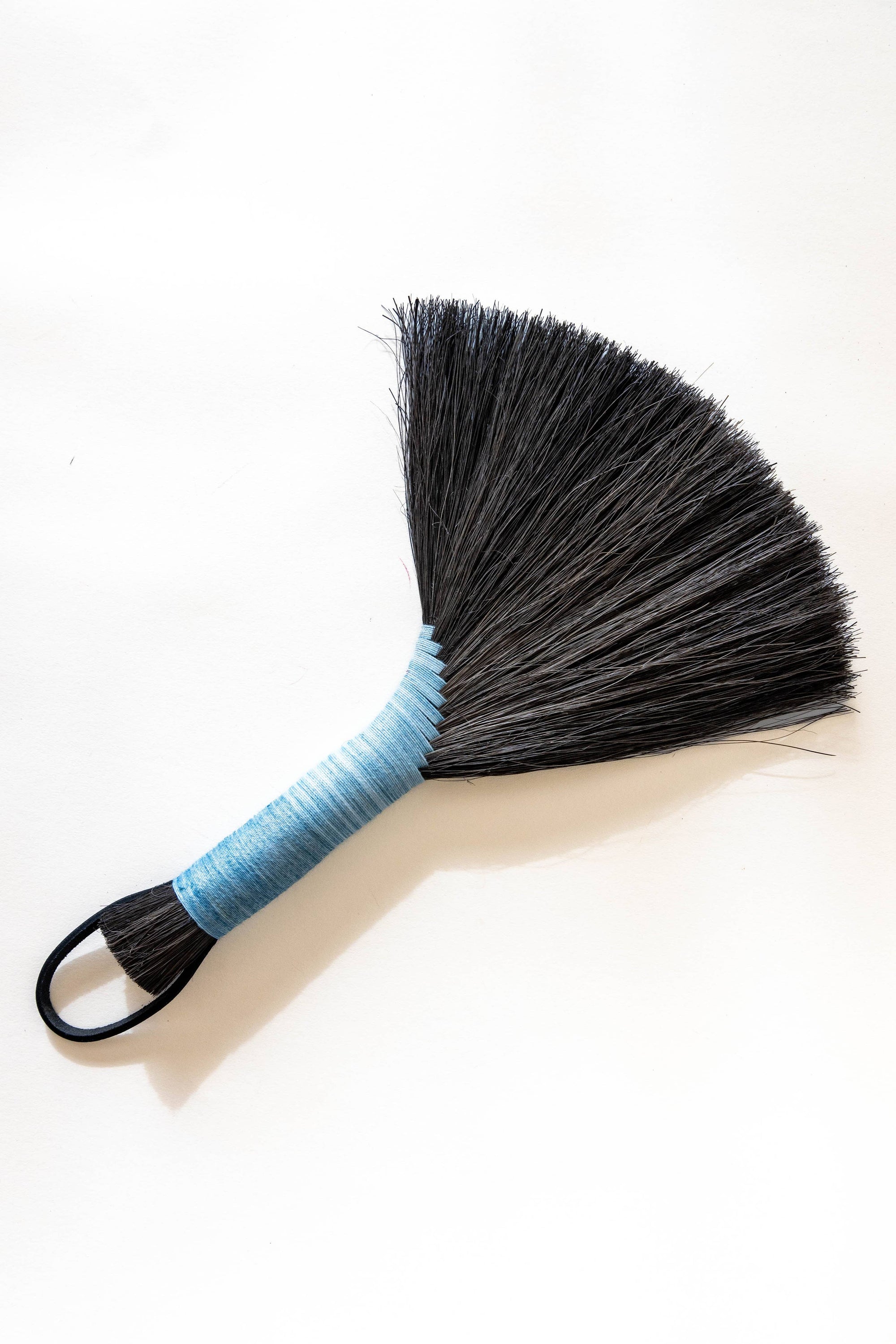 Tampico wing brush with dark bristles, light blue handle, and black leather cord loop