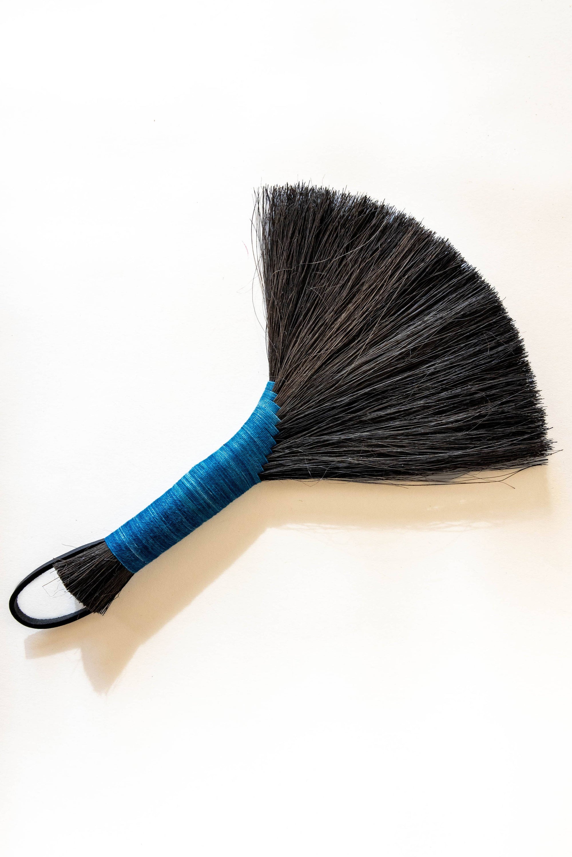 Hand broom with dark bristles, bright blue handle, black leather cord loop