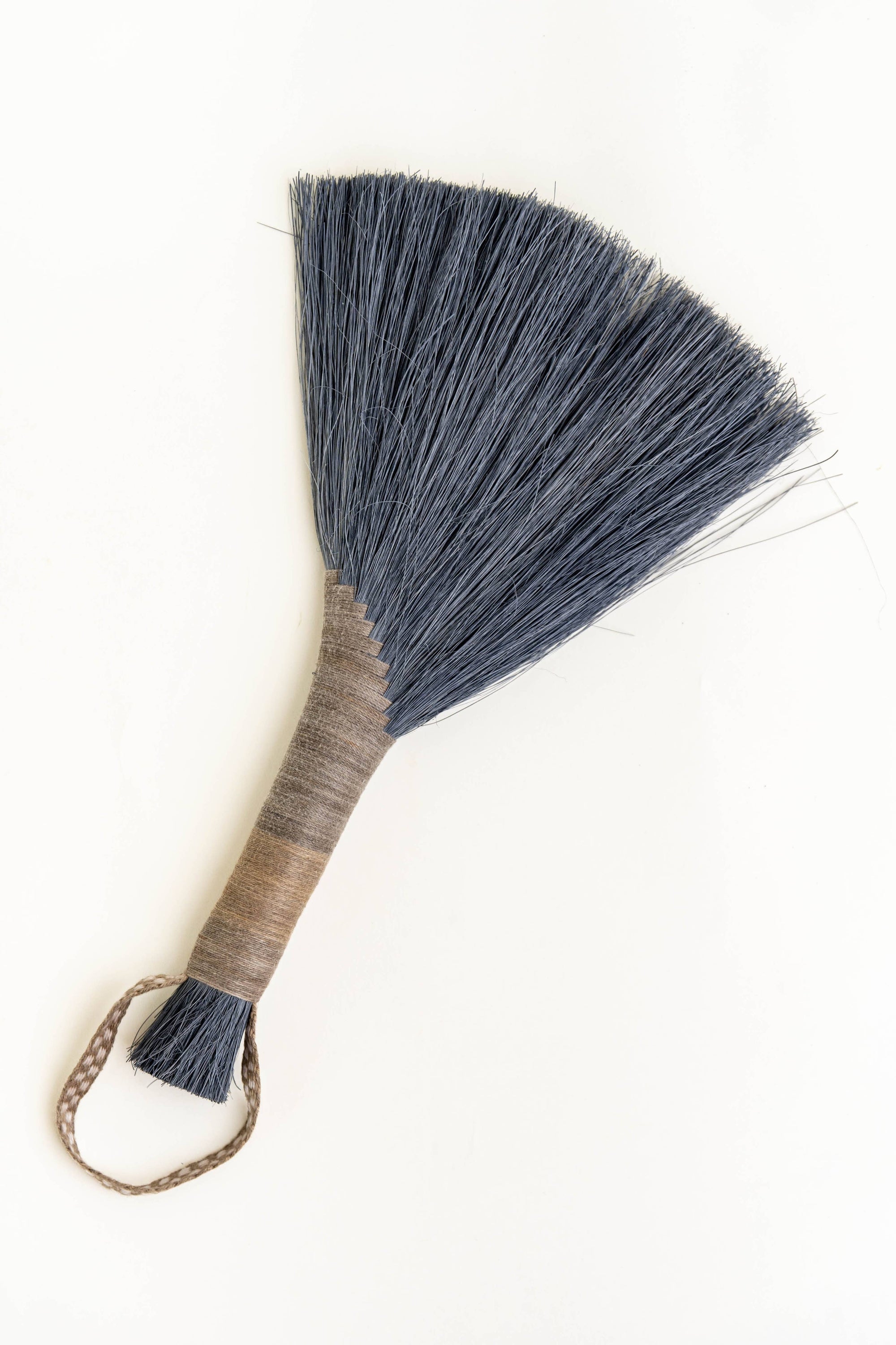 Handheld wing broom with dark gray fiber head, brown wrapped handle, and dark cord loop