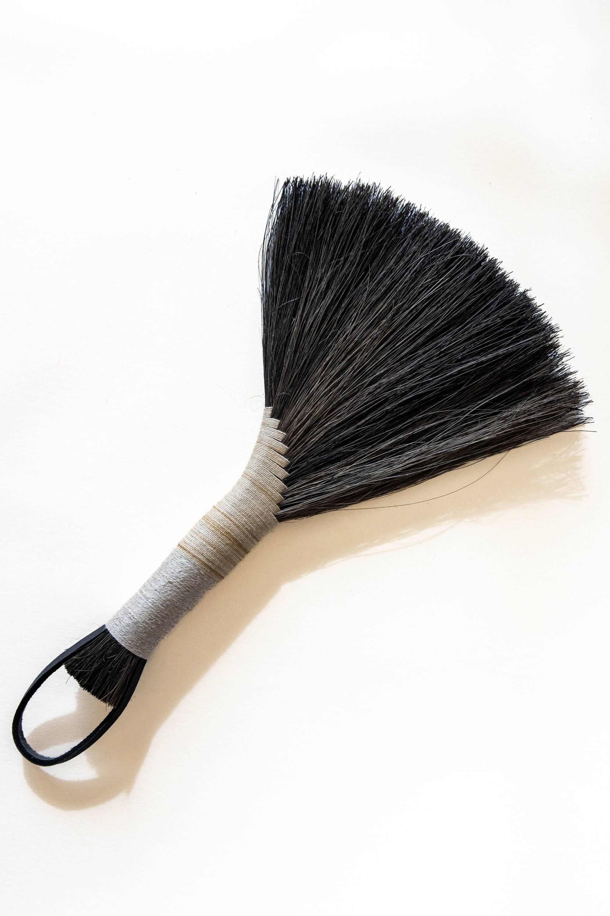 Hand broom with dark bristles, beige handle, black leather cord loop