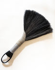 Hand broom with dark bristles, beige handle, black leather cord loop