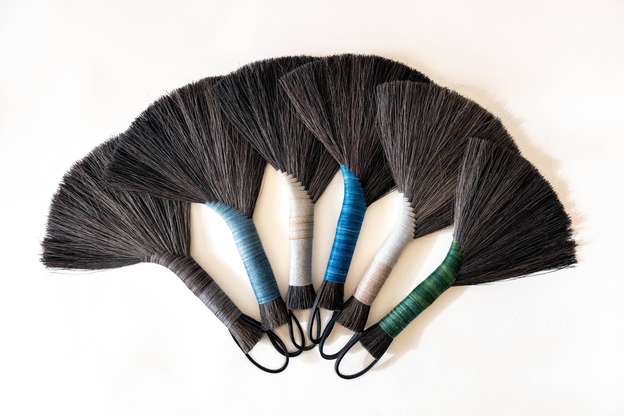 Set of hand brooms with black bristles, beige handles, blue accents, leather cord loops