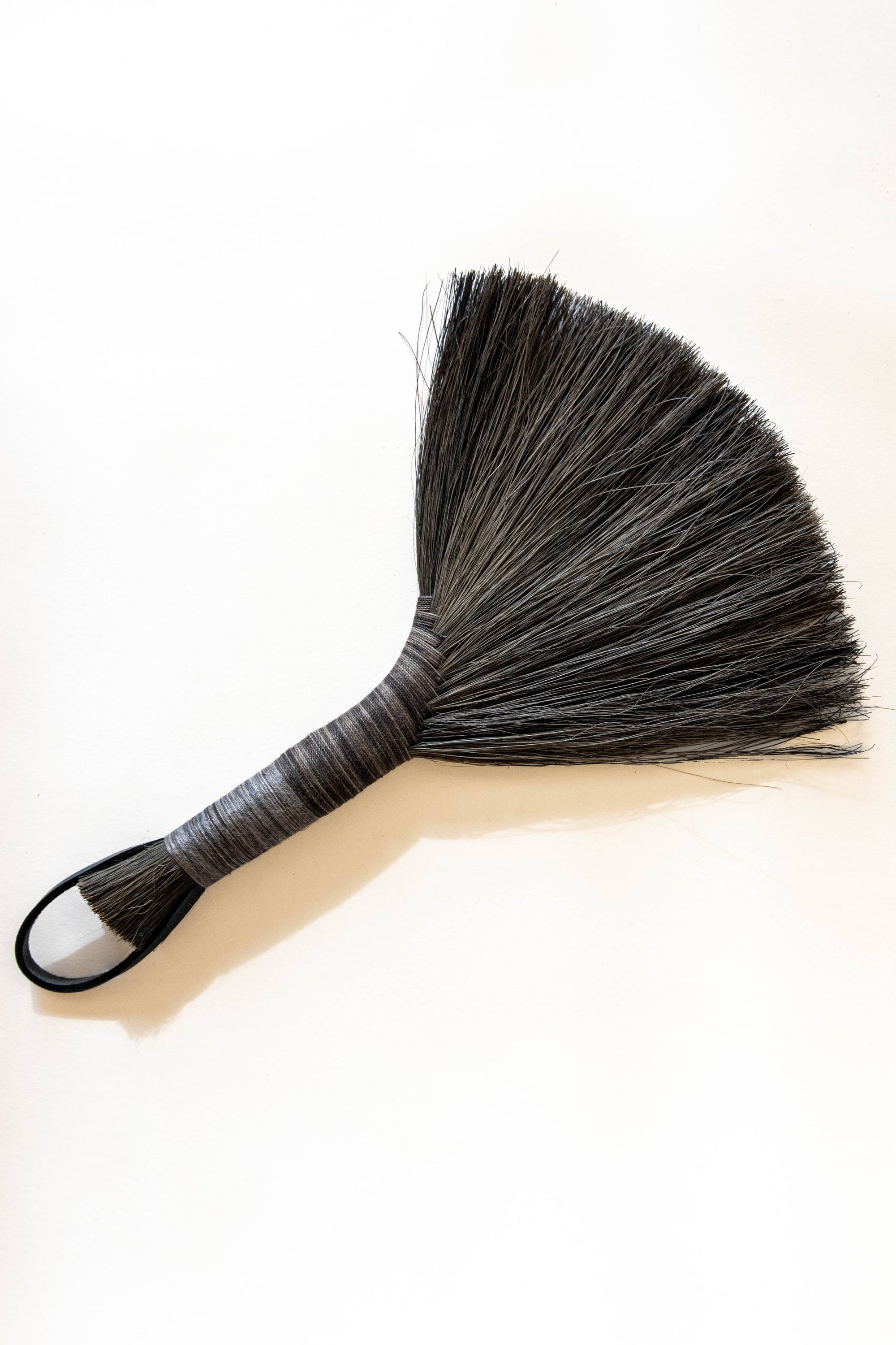 Hand broom with dark bristles, beige handle, black leather cord loop