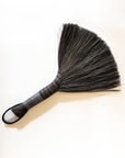Hand broom with dark bristles, beige handle, black leather cord loop