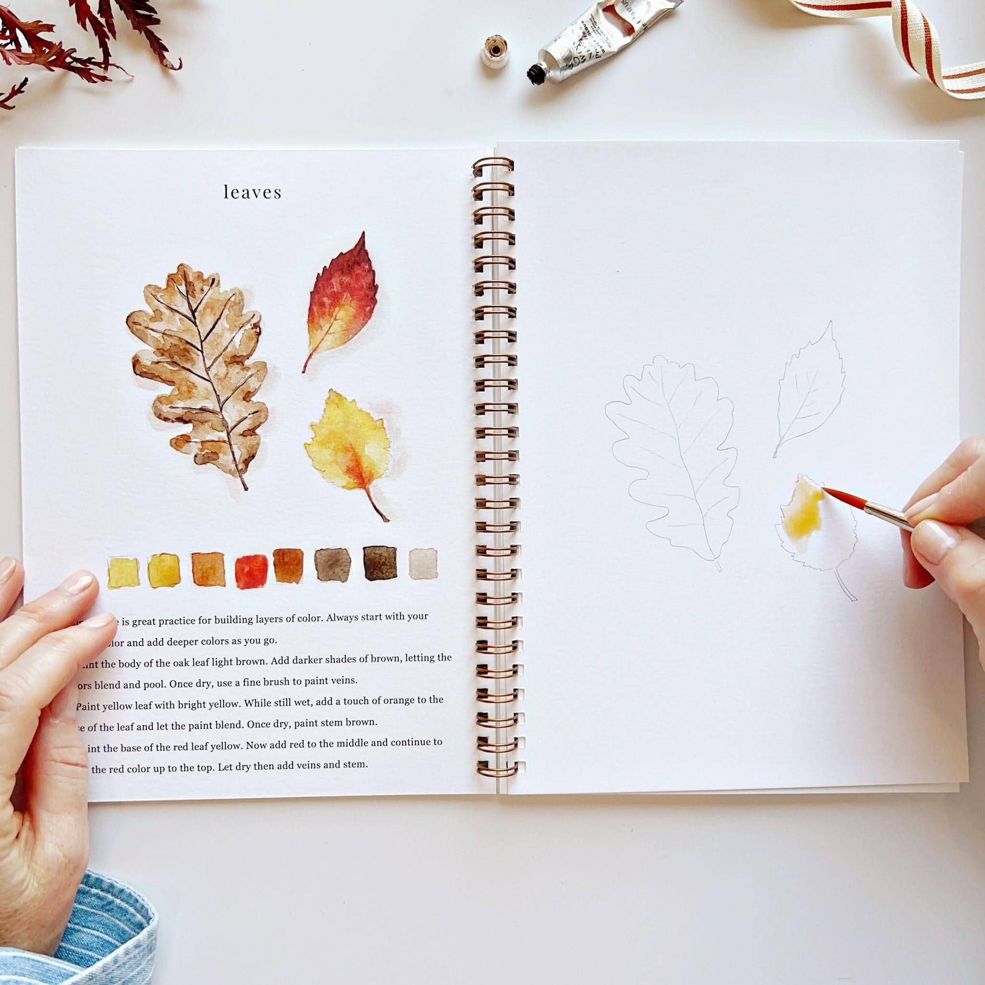 Autumn watercolor workbook open to leaf study page with watercolor samples and color swatches