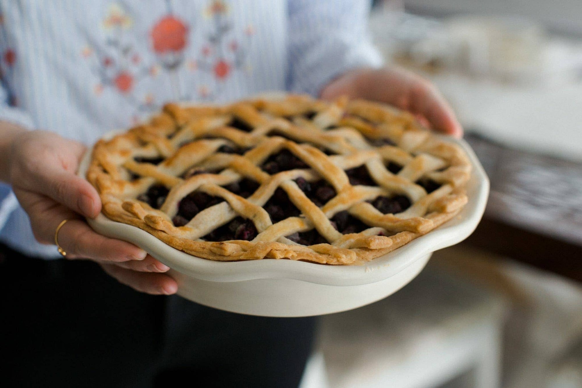 Frilly pie plate with a lattice pie, dark filling visible, held by hands