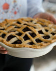 Frilly pie plate with a lattice pie, dark filling visible, held by hands
