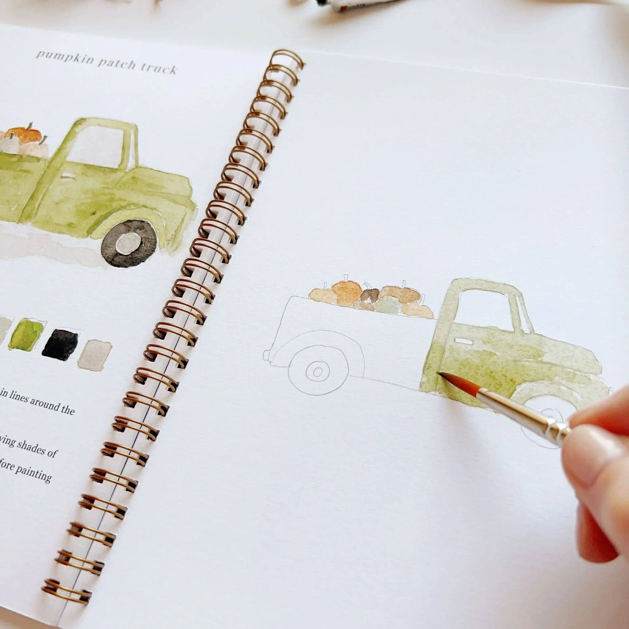 Autumn watercolor workbook close view of painted truck on page with brush in hand