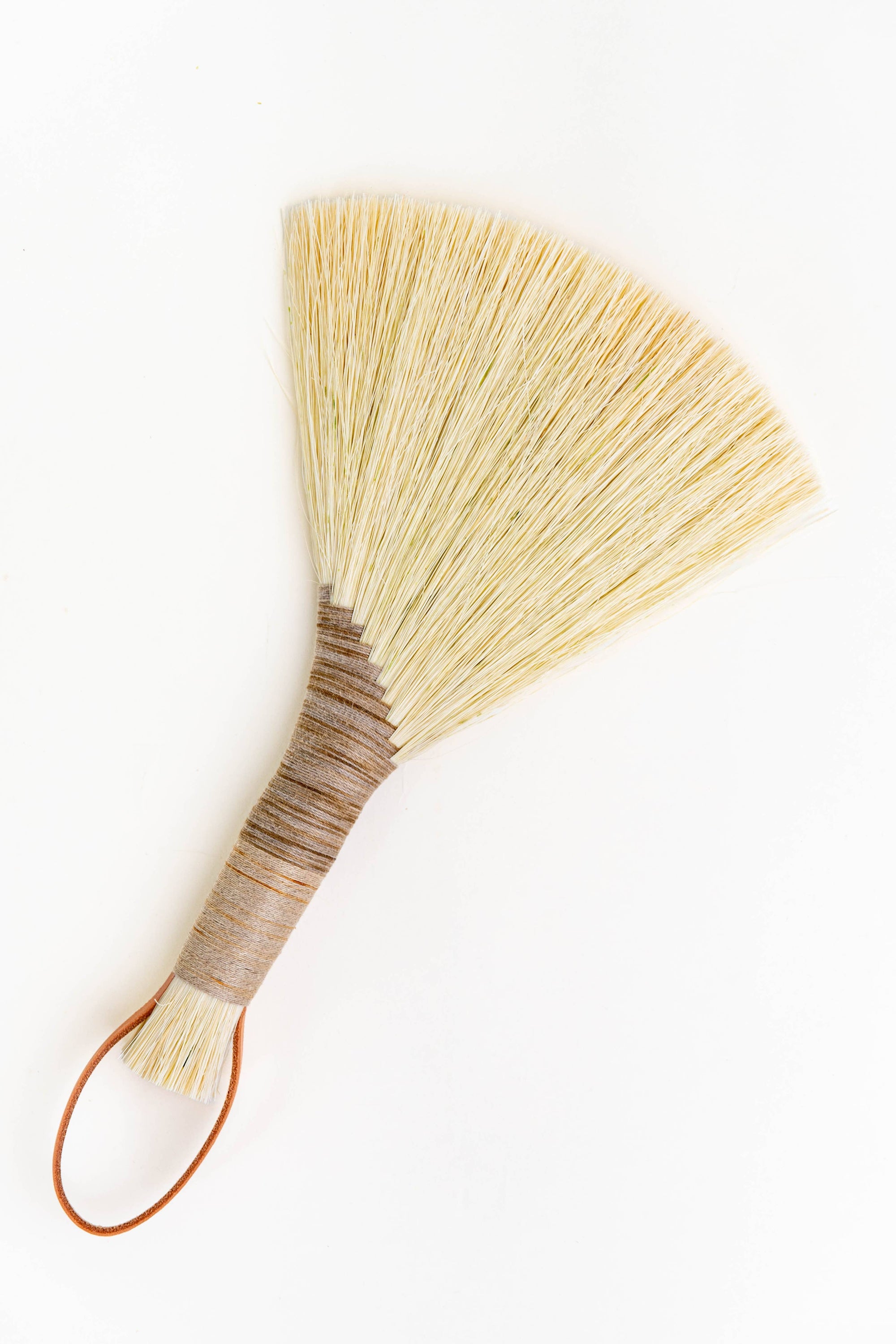 Handheld wing broom with light straw fiber head and brown leather cord loop