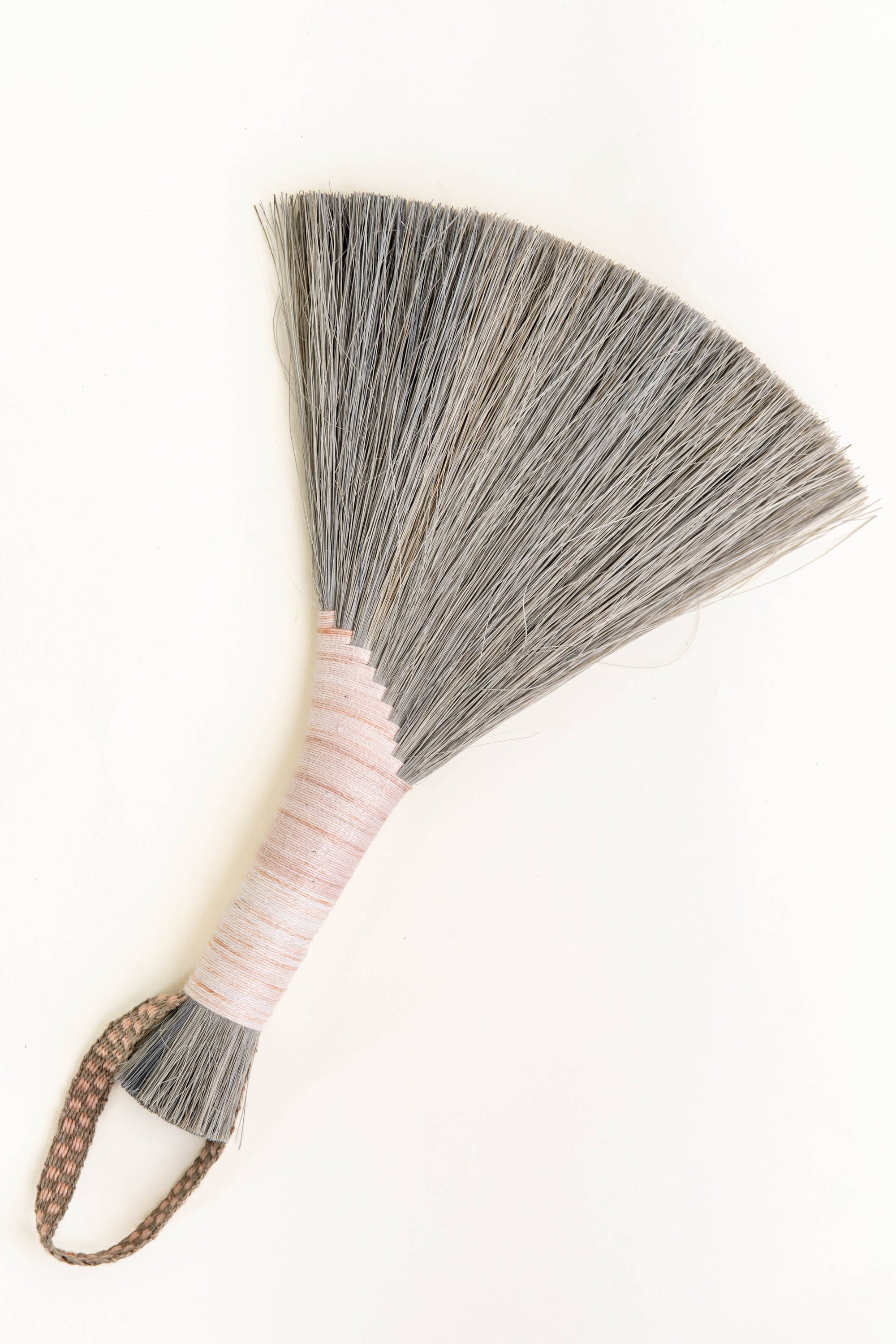 Handheld wing broom with gray fiber head, pale pink wrapped handle, and brown cord loop