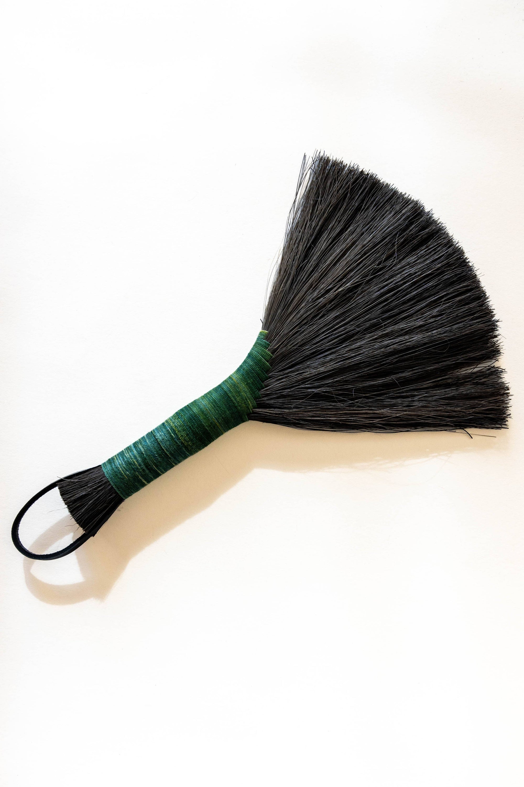 Hand broom with dark bristles, green-wrapped handle, black leather cord loop