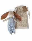 Rabbit plush doll with blue striped overalls beside a leaf-print drawstring bag